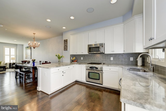 kitchen with backsplash, appliances with stainless steel finishes, a peninsula, white cabinets, and a sink