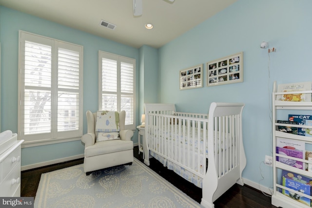 bedroom with visible vents, multiple windows, a crib, and wood finished floors