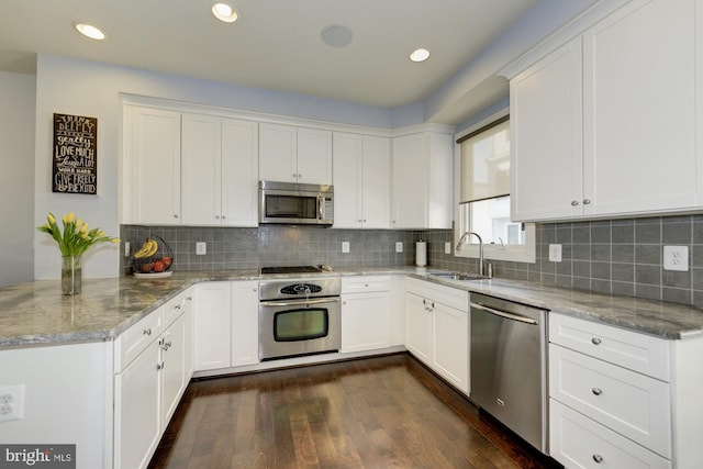 kitchen with tasteful backsplash, a sink, appliances with stainless steel finishes, a peninsula, and dark wood-style flooring