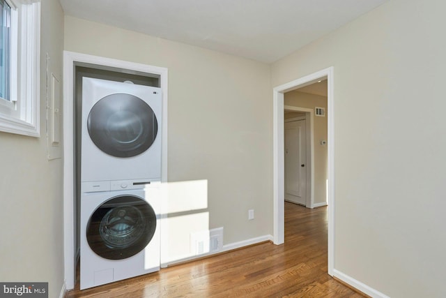 washroom with visible vents, stacked washer and clothes dryer, wood finished floors, baseboards, and laundry area