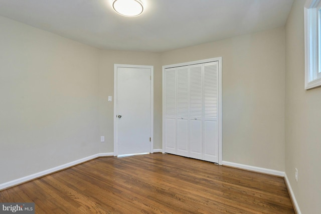 unfurnished bedroom with wood finished floors, baseboards, and a closet