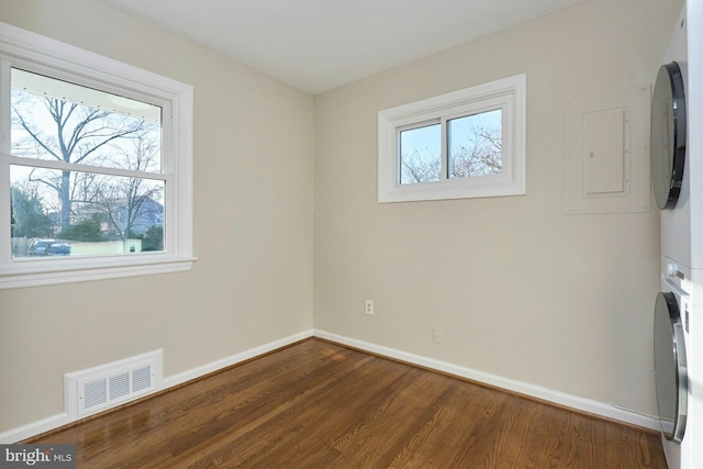 unfurnished room with dark wood finished floors, baseboards, visible vents, and stacked washing maching and dryer