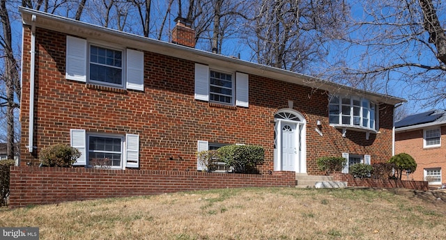 raised ranch with brick siding, a chimney, and a front yard