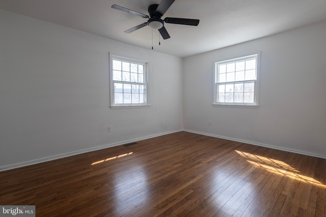 empty room featuring plenty of natural light, dark wood-style floors, visible vents, and baseboards