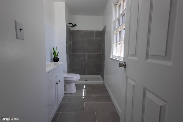 bathroom with toilet, tiled shower, tile patterned flooring, baseboards, and vanity