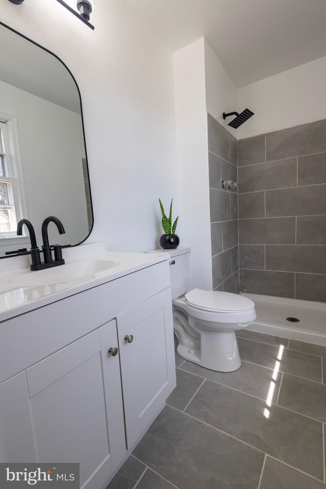 full bath featuring a tile shower, tile patterned floors, toilet, and vanity