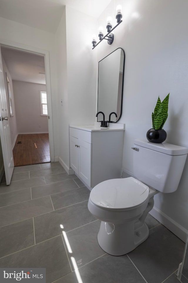 half bathroom with vanity, toilet, wood finished floors, and baseboards