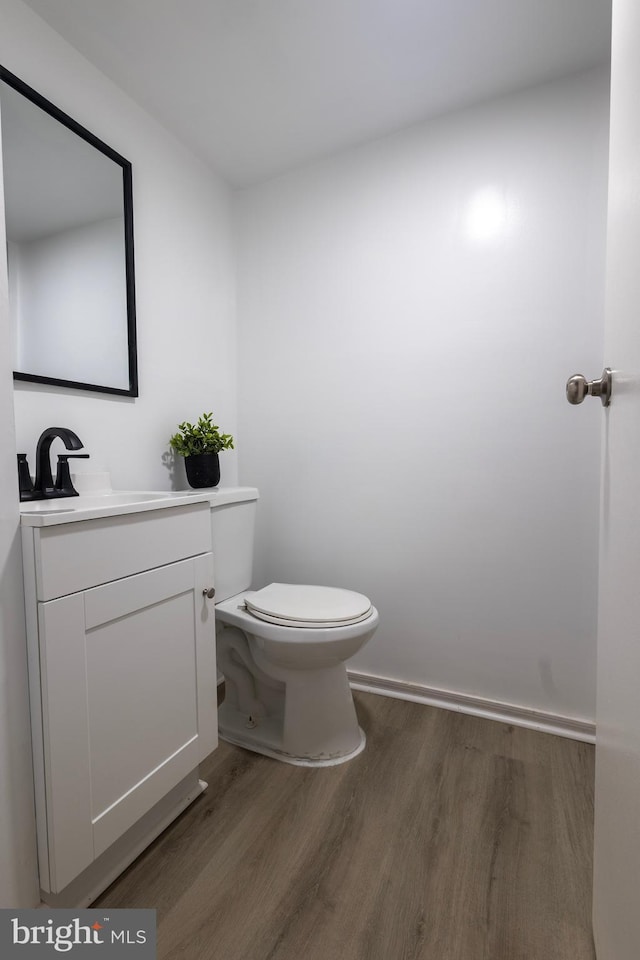 half bath with toilet, wood finished floors, and vanity