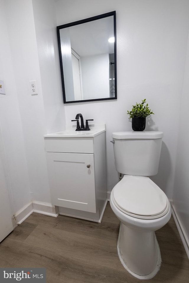 half bathroom with baseboards, wood finished floors, and vanity