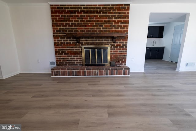 unfurnished living room with visible vents, a brick fireplace, a sink, and wood finished floors