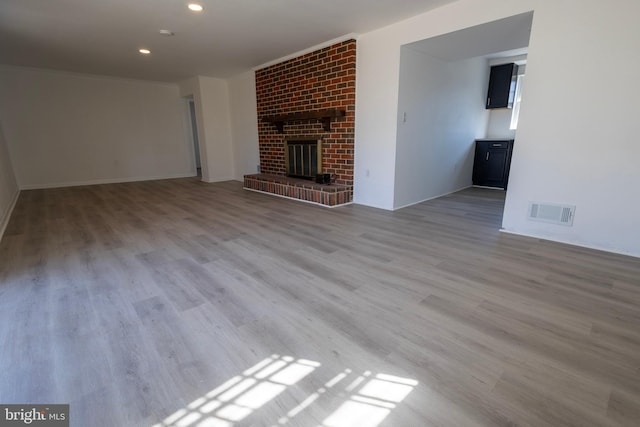 unfurnished living room featuring visible vents, recessed lighting, a brick fireplace, and wood finished floors