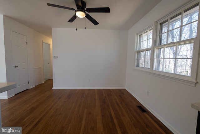 spare room featuring ceiling fan, visible vents, baseboards, and dark wood-style floors