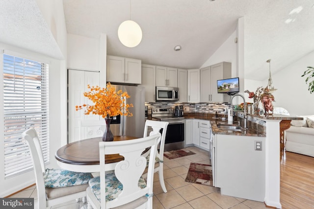 kitchen featuring lofted ceiling, a peninsula, light tile patterned flooring, a sink, and stainless steel appliances