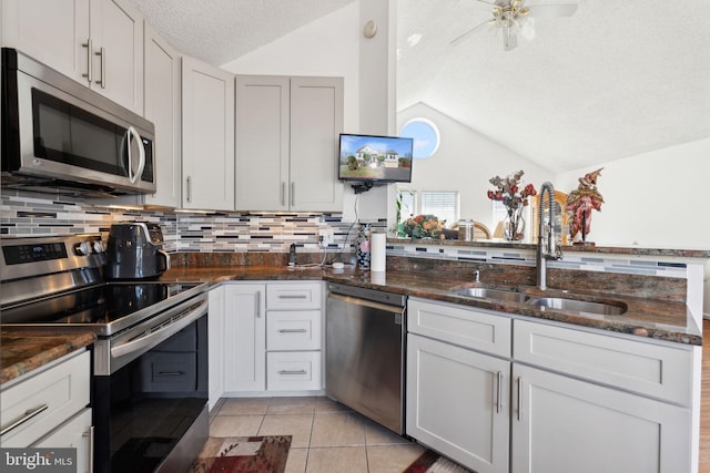 kitchen with lofted ceiling, light tile patterned floors, appliances with stainless steel finishes, a textured ceiling, and a sink