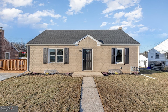 bungalow-style house with brick siding, a chimney, a front yard, and a shingled roof