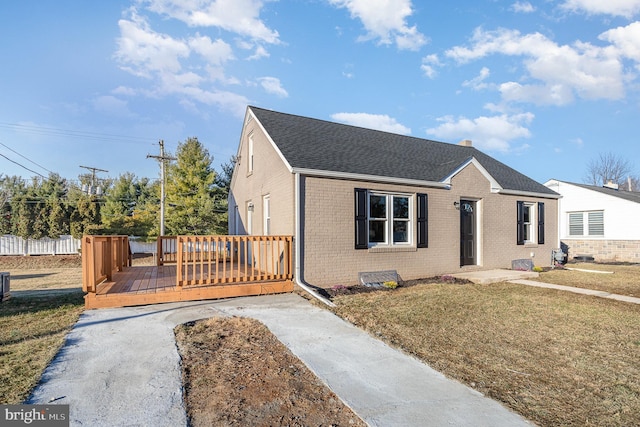 bungalow-style house featuring a deck, fence, roof with shingles, a front yard, and brick siding