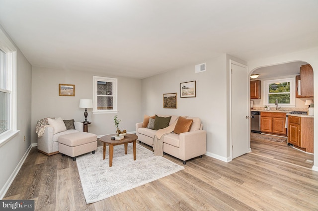 living room featuring visible vents, baseboards, arched walkways, and light wood-style flooring