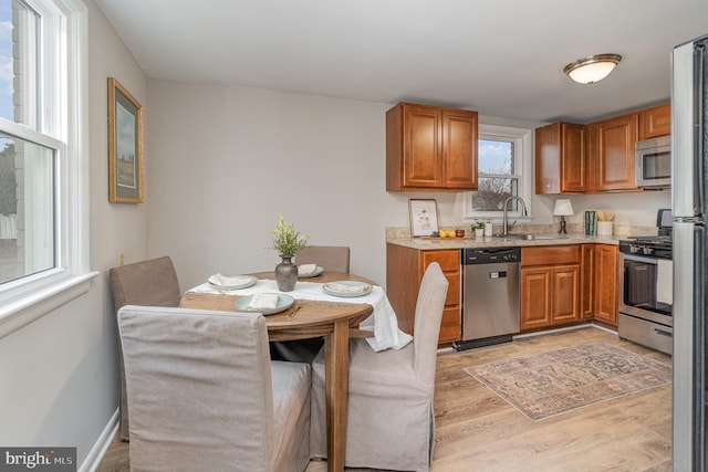 kitchen with a sink, stainless steel appliances, light countertops, light wood-style floors, and brown cabinets