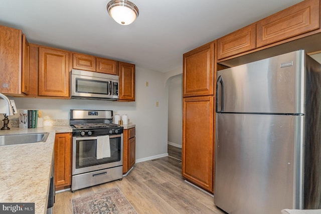 kitchen with a sink, arched walkways, appliances with stainless steel finishes, light wood finished floors, and light countertops