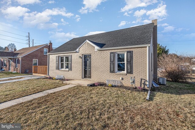 view of front facade with brick siding, central AC unit, a shingled roof, and a front lawn