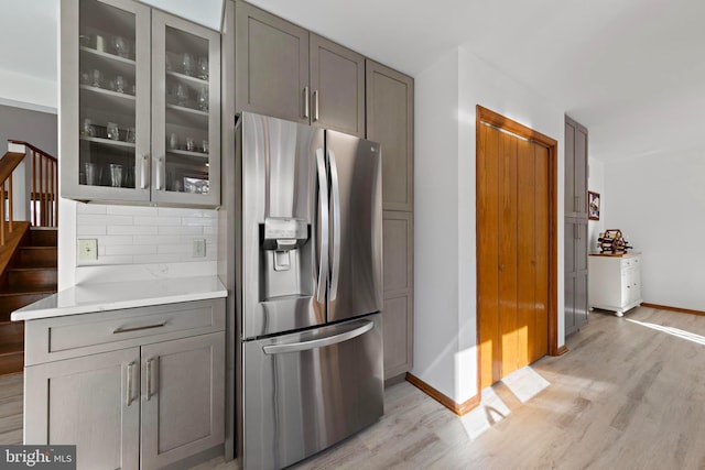 kitchen with decorative backsplash, light wood-type flooring, stainless steel fridge, and gray cabinetry