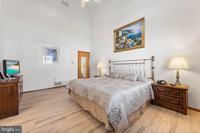 bedroom featuring visible vents, light wood-style flooring, baseboards, and a towering ceiling