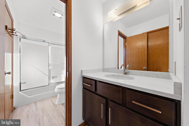 bathroom featuring shower / bath combination with glass door, toilet, wood finished floors, and vanity