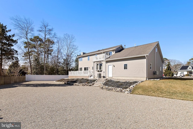 back of property with a yard, a balcony, and fence