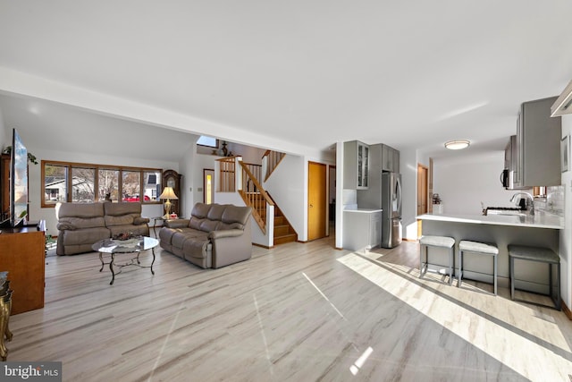 living area featuring vaulted ceiling, stairway, and light wood-style floors