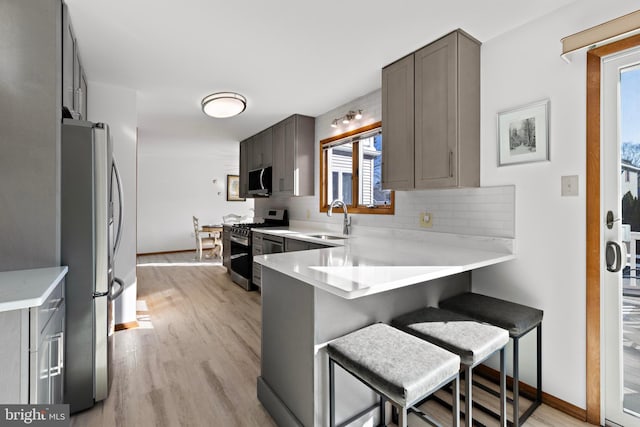 kitchen with a peninsula, a sink, decorative backsplash, light countertops, and appliances with stainless steel finishes