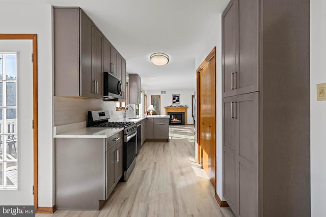 kitchen with a sink, tasteful backsplash, appliances with stainless steel finishes, light wood finished floors, and light countertops