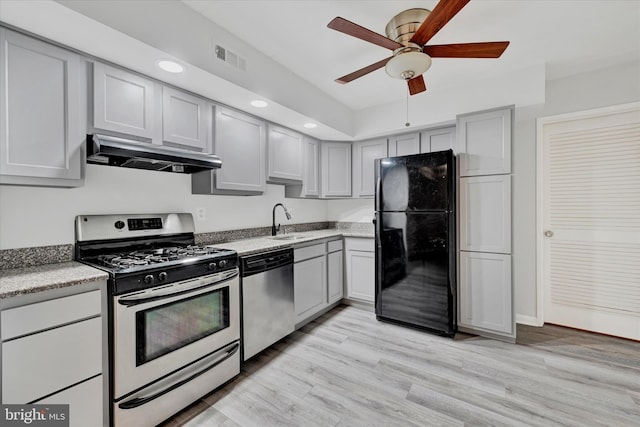 kitchen featuring visible vents, under cabinet range hood, a sink, light wood-style floors, and appliances with stainless steel finishes