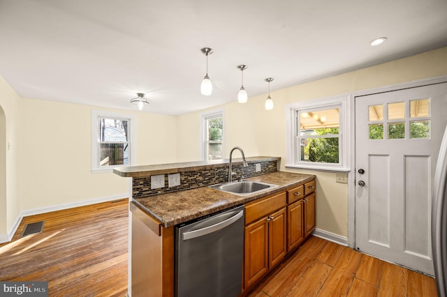 kitchen with visible vents, a peninsula, stainless steel dishwasher, brown cabinetry, and a sink