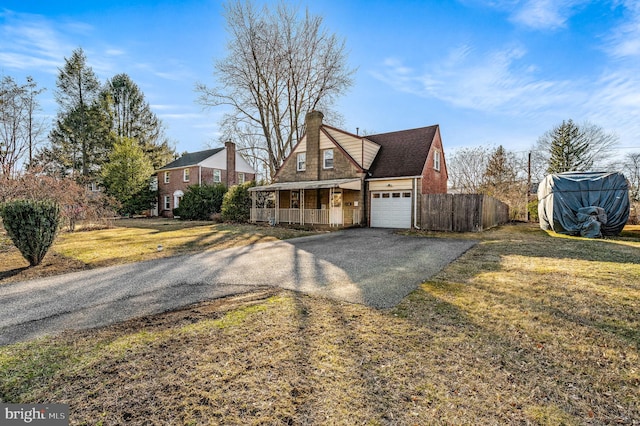 view of front of house with a front yard, covered porch, a chimney, a garage, and driveway