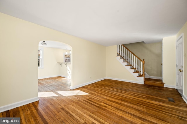 interior space with hardwood / wood-style floors, visible vents, baseboards, arched walkways, and stairs