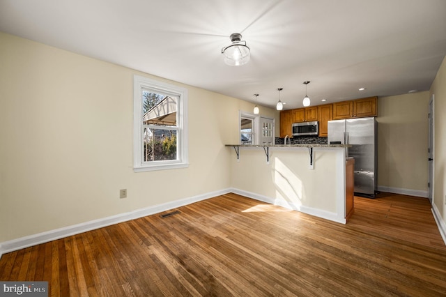 kitchen with visible vents, a breakfast bar, appliances with stainless steel finishes, a peninsula, and brown cabinetry