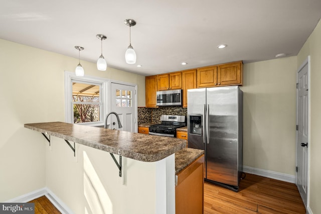 kitchen featuring a breakfast bar, a peninsula, stainless steel appliances, dark countertops, and tasteful backsplash