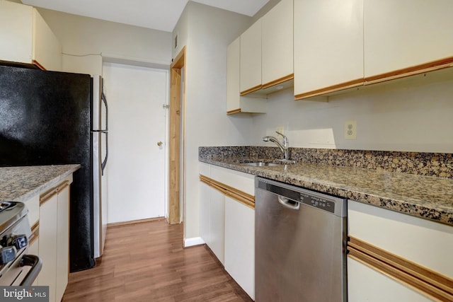 kitchen featuring light stone countertops, wood finished floors, a sink, appliances with stainless steel finishes, and white cabinetry