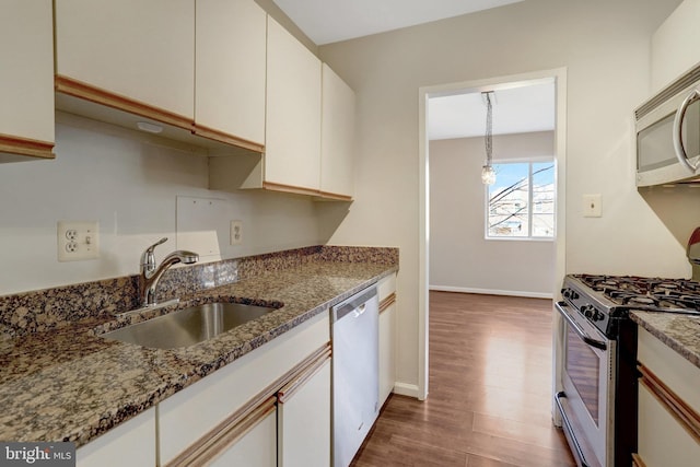 kitchen with a sink, wood finished floors, white cabinetry, appliances with stainless steel finishes, and light stone countertops