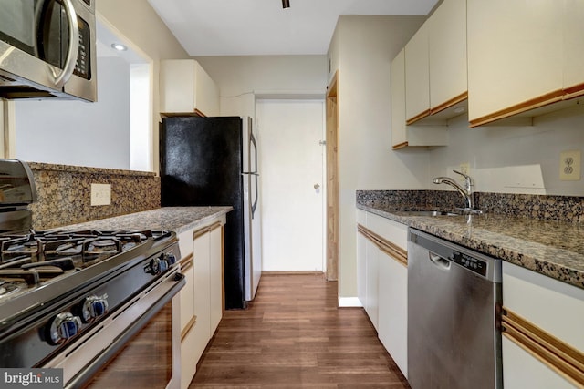 kitchen featuring a sink, backsplash, dark stone countertops, stainless steel appliances, and dark wood-style flooring