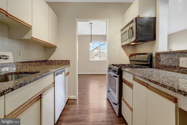 kitchen with a sink, dark wood-style floors, stainless steel appliances, dark stone counters, and baseboards