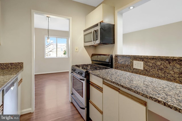 kitchen with wood finished floors, dark stone counters, appliances with stainless steel finishes, white cabinets, and baseboards