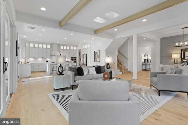 living room featuring light wood-type flooring, visible vents, beam ceiling, and stairway