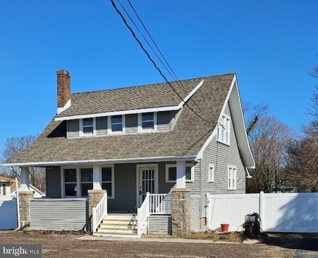 view of front of house with a shingled roof, fence, covered porch, and a chimney