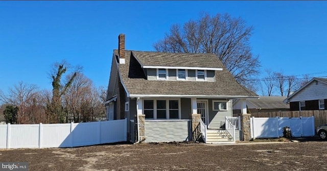 view of front of house featuring roof with shingles, covered porch, a chimney, and fence