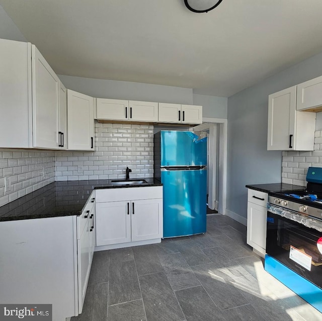 kitchen with stainless steel gas range oven, dark countertops, freestanding refrigerator, white cabinets, and a sink