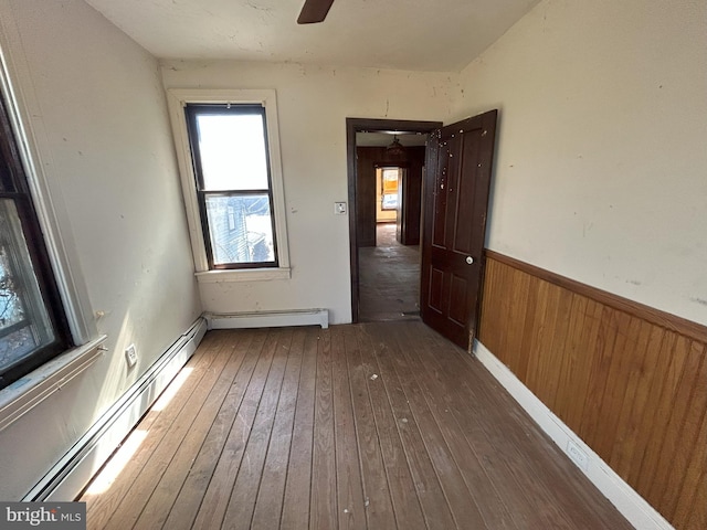 unfurnished room featuring a baseboard radiator, wooden walls, wainscoting, and hardwood / wood-style flooring