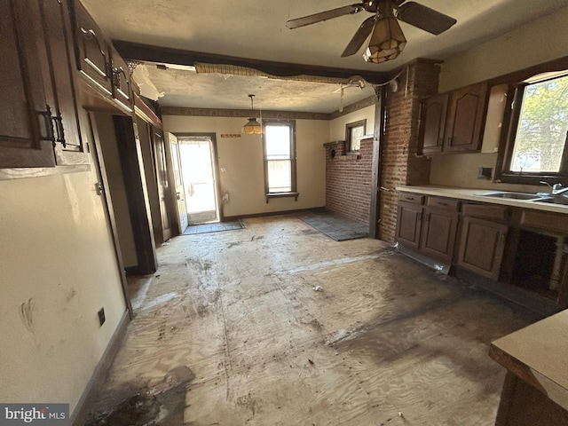 kitchen with a sink, light countertops, baseboards, dark brown cabinets, and hanging light fixtures