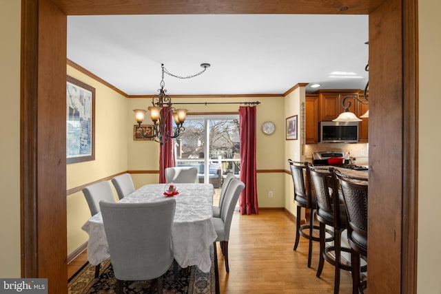 dining space featuring light wood finished floors, a chandelier, baseboards, and ornamental molding