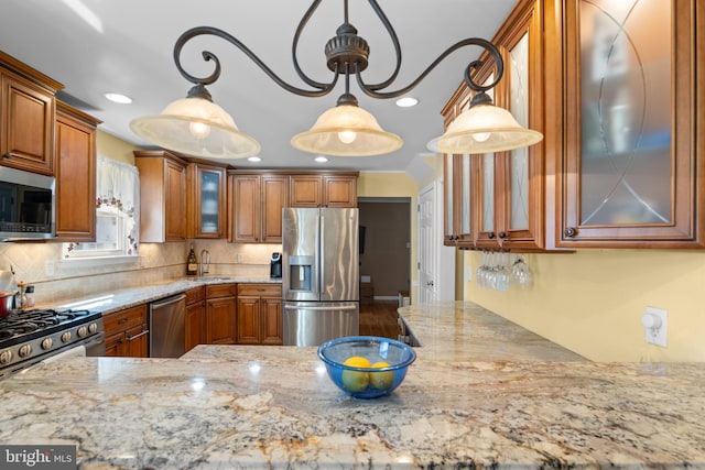 kitchen featuring brown cabinetry, stainless steel appliances, light stone counters, and a sink